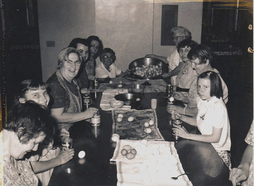 Women and children around a table are dyeing Easter eggs