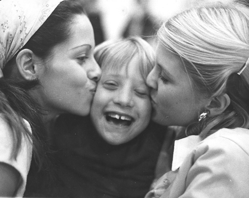 Two girls kiss each cheek of a young boy